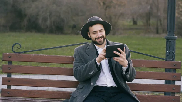 Hipser tvůrčí obchodní muž v klobouku pomocí počítače tablet pc a sedí na městské ulici lavičce v parku během přestávky — Stock fotografie