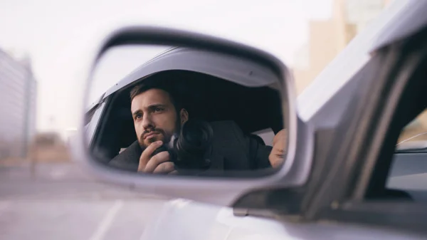 Réflexion dans le miroir latéral du jeune détective privé assis à l'intérieur de la voiture et photographier avec un appareil photo dslr — Photo