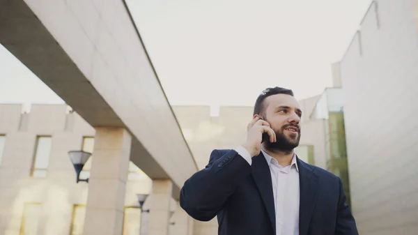 Üzleti ember beszél a mobiltelefon foglalkozik, és a gyaloglás közelében modern irodaházak — Stock Fotó