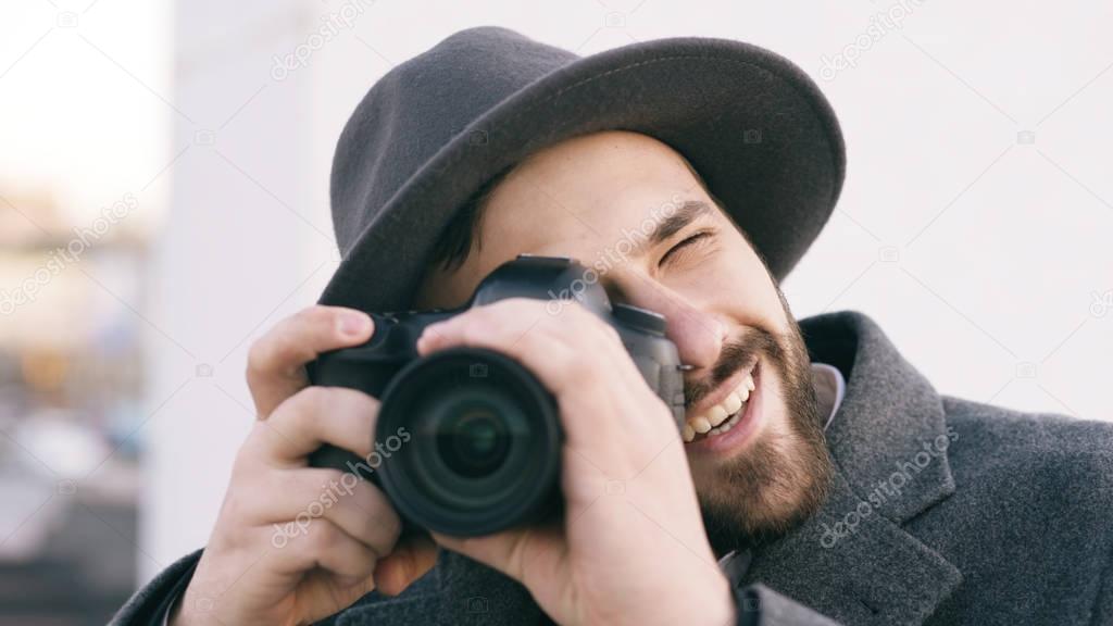 Closeup of happy paparazzi man in hat photographing celebrities on camera and smiling outdoors