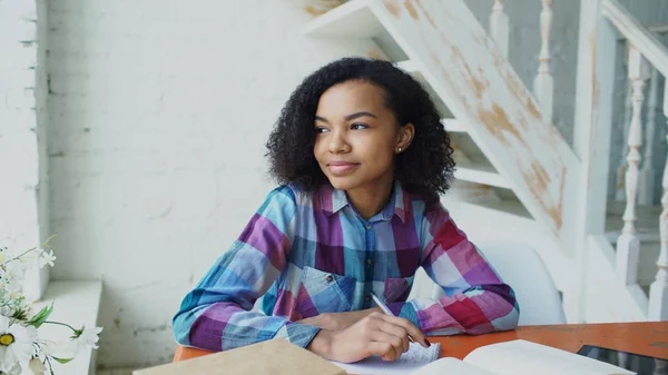 Junges Mädchen mit lockigem Haar und gemischter Rasse, das am Tisch sitzt und konzentrierte Lektionen für die Prüfung zur Universität konzentriert — Stockfoto