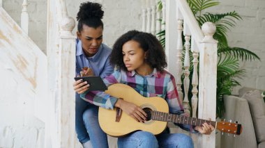 Akustik gitar evde oynamak için genç kız kardeşi öğretim merdivenlerde oturan karışık yarış genç kadın