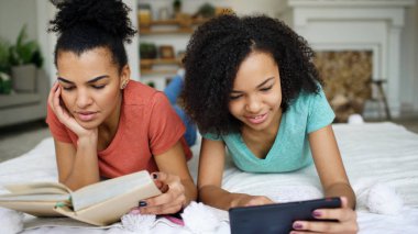 Karışık neşeli iki kitap okuma ve tablet bilgisayar görüşmeler kullanarak komik kız yarış ve evde yatakta yatan iyi eğlenceler