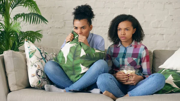 Zwei gemischte Rasse lockige Freundinnen sitzen auf der Couch und sehen sehr beängstigende Film im Fernsehen und essen Popcorn zu Hause — Stockfoto