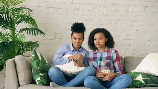 Zwei gemischte Rasse lockige Freundinnen sitzen auf der Couch und sehen sehr beängstigende Film im Fernsehen und essen Popcorn zu Hause — Stockfoto