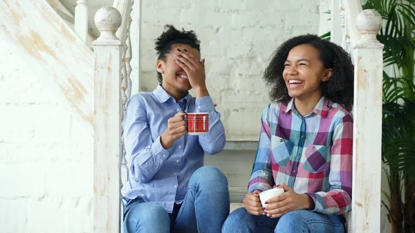 Duas meninas afro-americanas encaracoladas se sentam nas escadas se divertem rindo e conversando juntas em casa — Fotografia de Stock