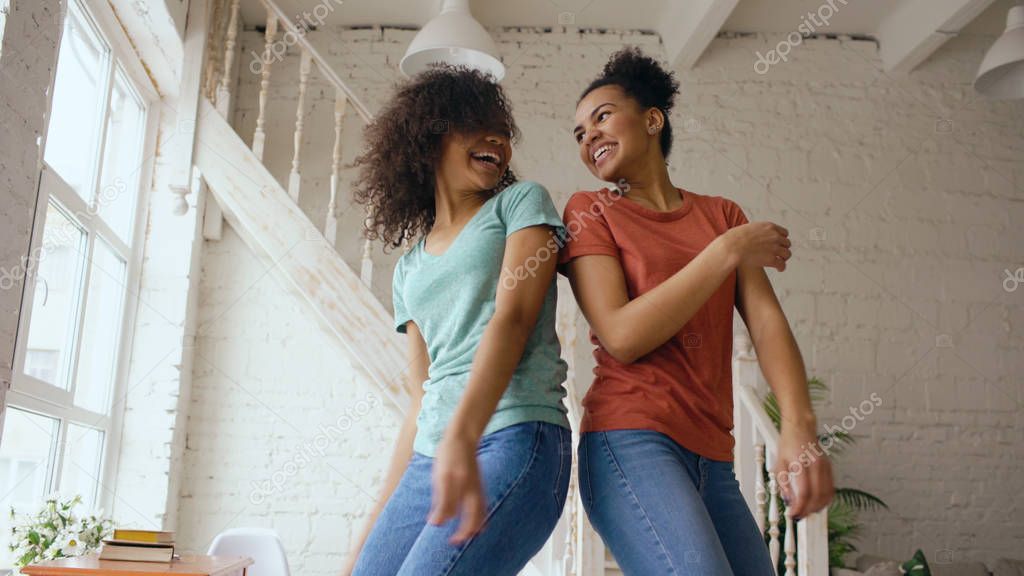 Mixed race young beautiful girls dancing on a bed together having fun leisure in bedroom at home