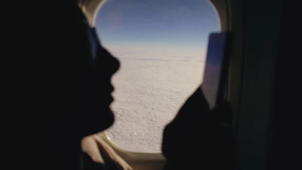 Силуэт крупным планом женщина сидит возле окна самолета с помощью мобильного телефона во время полета — стоковое фото