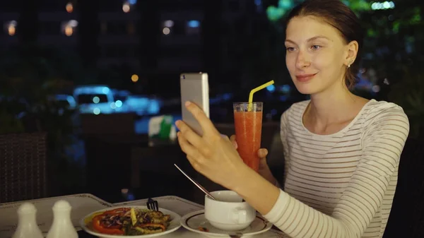 Mutlu kadın ateş smartphone ve drinck kullanarak selfie kokteyl suyu gece restoranda oturan — Stok fotoğraf