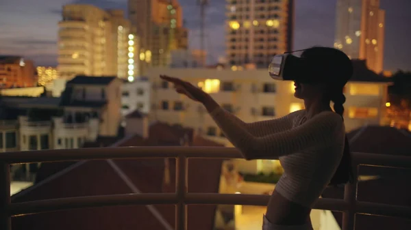 Young woman on rooftop terrace using virtual reality headset and having VR experience at night — Stock Photo, Image