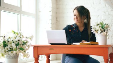 Dizüstü bilgisayar ve yazma kitap kapalı kafede oturan genç güzel kadın öğrenci