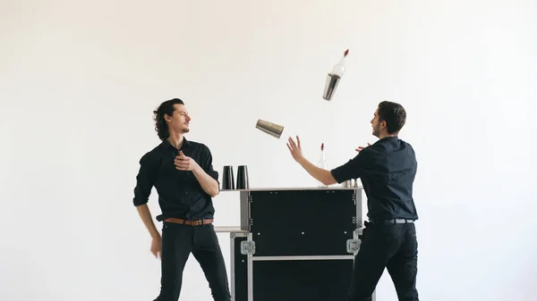 Професійні бармени-чоловіки жонглюють пляшки і трясуть коктейль на мобільному барному столі на білому фоні студії в приміщенні — стокове фото