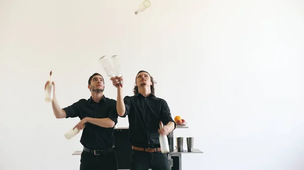 Професійні бармени-чоловіки жонглюють пляшки і трясуть коктейль на мобільному барному столі на білому фоні студії в приміщенні — стокове фото