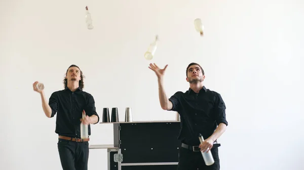 Professinal bartender men juggling bottles and shaking cocktail at mobile bar table on white background studio indoors — Stock Photo, Image