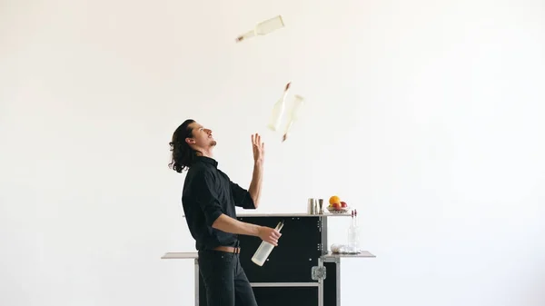 Professinal bartender man juggling bottles and shaking cocktail at mobile bar table on white background — Stock Photo, Image