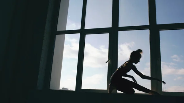 Silhouette of young girl dancer perfomance contemporary dance on windowsiil in dance studio indoors — Stock Photo, Image