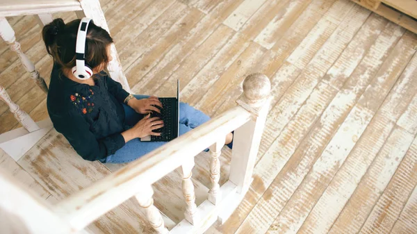 Bovenaanzicht van vrouw met hoofdtelefoon ontspannen met laptop zittend op de trap in de woonkamer bij u thuis — Stockfoto