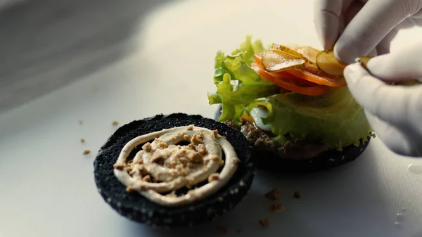 Primer plano de cocinero a la parrilla hamburguesa negra con salsa y verduras en el tablero de la cocina — Foto de Stock