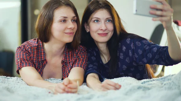 Две счастливые женщины друзья лежат в постели и делают селфи утром и весело провести время в постели — стоковое фото