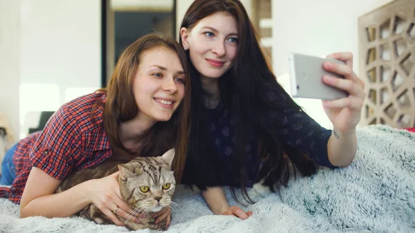 Dwóch przyjaciół szczęśliwa Kobieta, leżąc w łóżku i podejmowania selfie z cat i zabawy na łóżku w domu — Zdjęcie stockowe