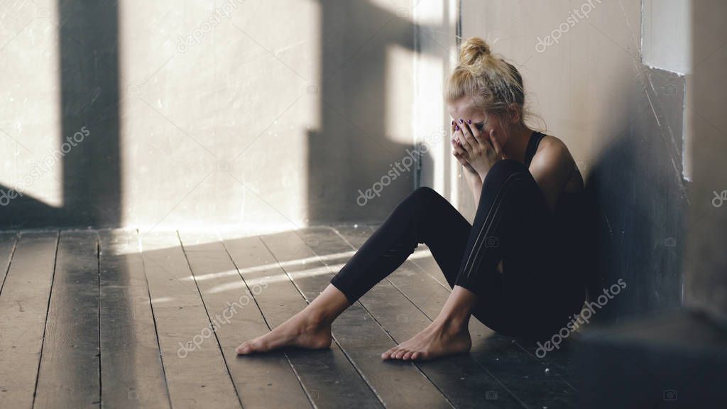 Closeup of young teenage girl dancer crying after loss perfomance sits on floor in hall indoors