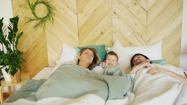 Jeune garçon drôle se réveiller pendant que ses parents dorment le matin sur le lit dans leur maison — Photo