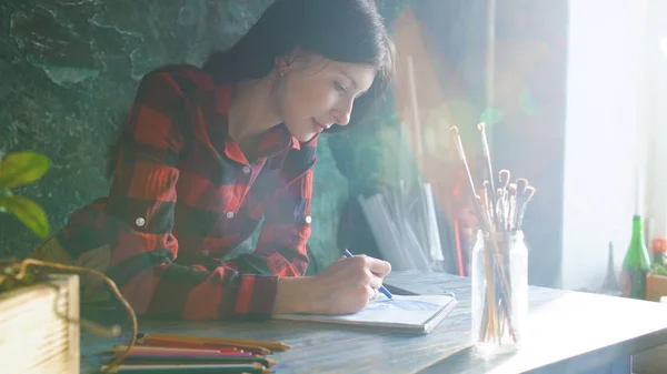 Jeune femme artiste peinture croquis sur carnet de papier avec crayon. Éclat de soleil lumineux de la fenêtre — Photo