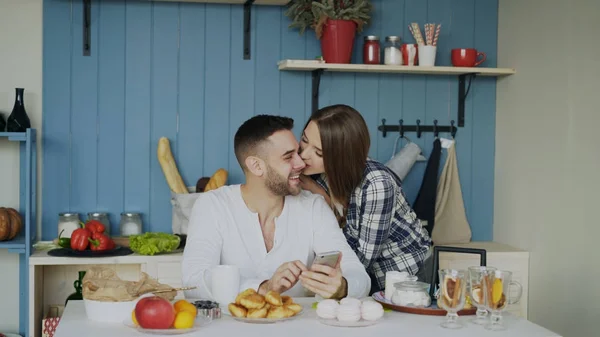 Attraktives Paar trifft sich zum Frühstück in der Küche und surft zu Hause mit dem Smartphone in den sozialen Medien — Stockfoto
