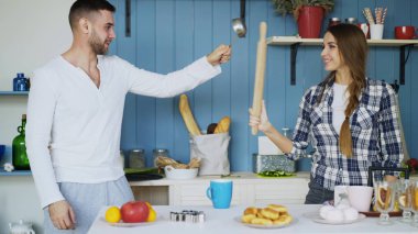 Mutlu çift mutfakta kepçe ve haddeleme pin ile evde kahvaltı yemek yaparken eskrim eğleniyor