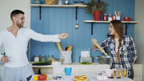 Glückliches Paar, das mit Schöpfkelle und Nudelholz Spaß in der Küche hat, während es zu Hause frühstückt — Stockfoto
