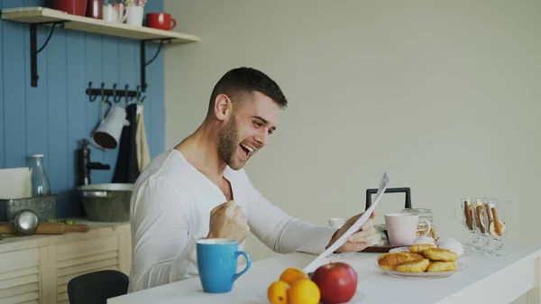 Красивий чоловік отримує хороші новини читання листа на кухні, поки сніданок вдома рано вранці — стокове фото