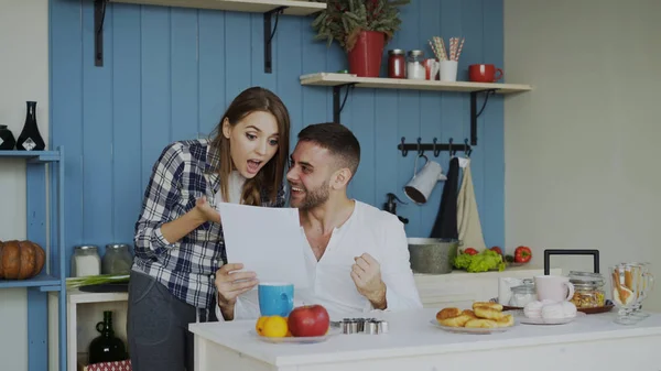 Приваблива щаслива пара отримує хороші новини, що розгортаються лист на кухні під час сніданку вдома — стокове фото