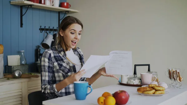 Ung glad kvinna överraskade för att få bra nyheter läsa brev i köket medan har frukost hemma tidigt på morgonen — Stockfoto