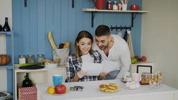 Привлекательная счастливая пара получает хорошие новости разворачиваясь письмо на кухне во время завтрака дома — стоковое фото