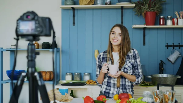 Молодая привлекательная женщина записывает видеоблог о кулинарии на камеру на кухне — стоковое фото
