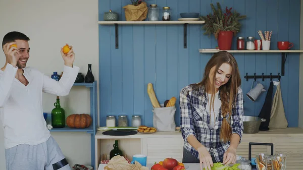 Привлекательная любящая пара, развлекающаяся на кухне. Красивый мужчина жонглирует фруктами, чтобы произвести впечатление на свою девушку — стоковое фото