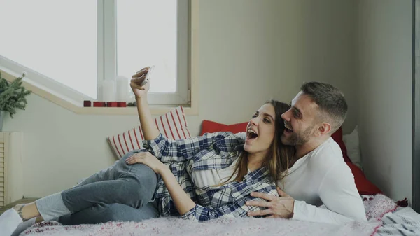 Casado casal feliz tomando portrain selfie enquanto deitado na cama em casa pela manhã — Fotografia de Stock