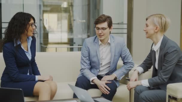 Businessman talking and duscussing future contract with female business partners sitting on couch in meeting room — Stock Video