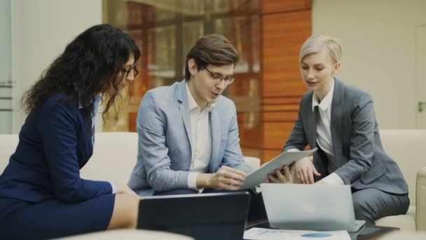 Businessman in glasses talking and duscussing future contract with female business partners sitting on couch in meeting room — Stock Video