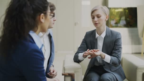 Empresaria hablando y duscussing futuro contrato con socios de negocios sentados en el sofá en el moderno centro de oficinas — Vídeo de stock