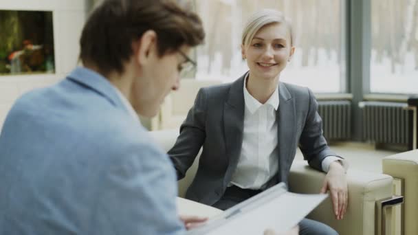 Businesswoman talking and duscussing company finance information with male business partner sitting on armchair in meeting room — Stock Video