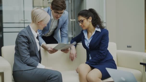 Tilt up of Cheerful businessman talking and discussing about financial report with business female colleagues sitting on sofa in meeting room — Stock Video