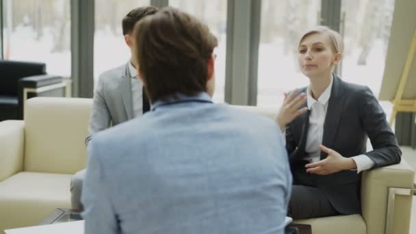 Panning shot di donna d'affari parlare e duscussing con colleghi di lavoro maschili seduti sul divano in una moderna sala ufficio — Video Stock