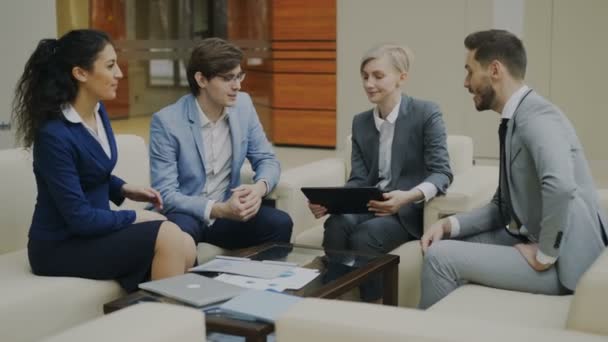 Empresária com tablet digital conversando com colegas de negócios masculinos e femininos sentados no sofá no escritório moderno — Vídeo de Stock