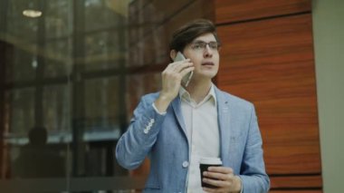 Stedicam atış smartphone ile konuşmak ve modern ofis salonunda yürüyüş neşeli işadamı