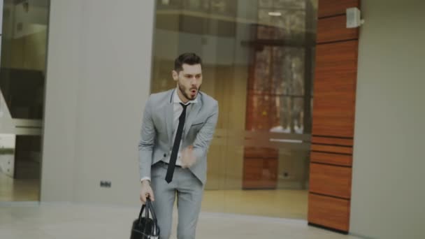 Счастливый и веселый бизнесмен с портфелем танцует в офисном холле, пока никто не смотрит его — стоковое видео