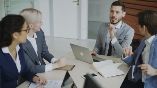 Исполнительный менеджер обсуждает бизнес-план с коллегами, сидящими за столом в конференц-зале — стоковое видео
