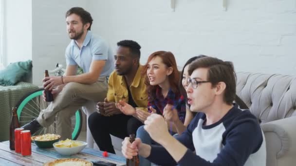 Multiethnische Gruppe befreundeter Sportfans, die gemeinsam ein Sportereignis im Fernsehen verfolgen, Snacks essen und an Feiertagen zu Hause Bier trinken — Stockvideo