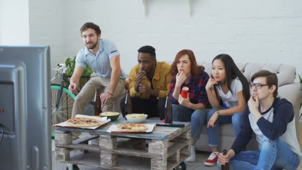 Fiatal baráti nézni olimpiai játékok felel meg a TV-ben együtt ételeket eszik, és iszik sört. Néhány közülük a győztes csapat, de mások csalódott boldog — Stock videók