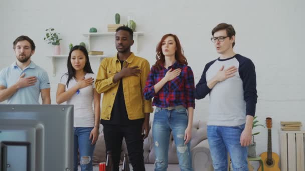 Multi-etnische groep van vrienden sportfans zingen volkslied voor sport kampioenschap op Tv kijken samen thuis — Stockvideo